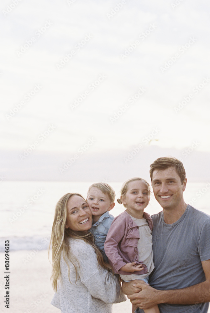 Couple standing with their son and daughter on a sandy beach by the ocean, looking at camera, smiling. Couple standing with their son and daughter on a sandy beach by the ocean, looking at camera, smiling.
