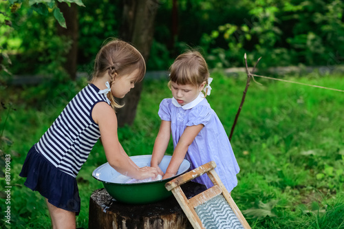 фотографія little helper girls sisters washes clothes using the washboard o