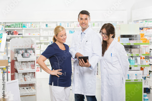 Confident Pharmacist Using Digital Tablet With Coworkers