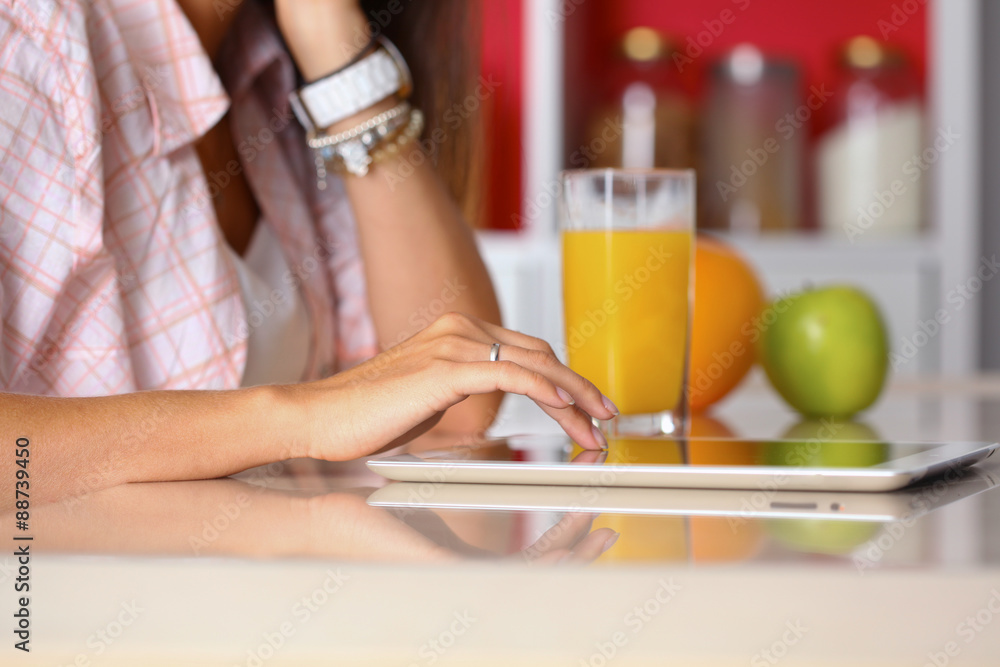 Woman using a tablet computer while drinking tea in her kitchen Woman using a tablet computer while drinking tea in her kitchen