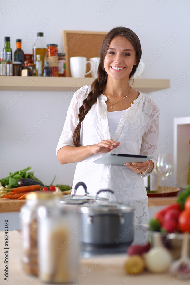 Young woman using a tablet computer to cook in her kitchen Young woman using a tablet computer to cook in her kitchen