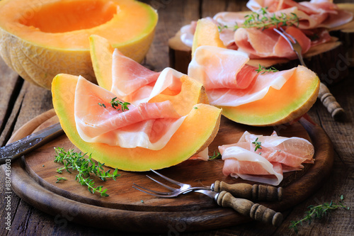 Italian prosciutto with melon with fresh thyme on rustic wooden kitchen table