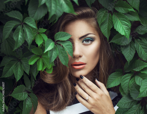 exy Beauty Girl with coral Lips. Provocative green Make up. Luxury Woman with Green Eyes. Fashion Brunette Portrait in wild leaves (grapes),  natural background. Gorgeous Woman Face. Long Hair photo