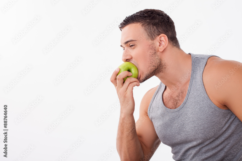 Cheerful young guy is biting a fruit greedily Cheerful young guy is biting a fruit greedily