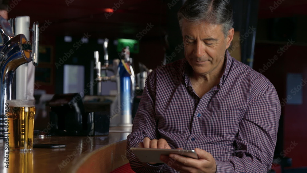Man having a pint at the bar using tablet Man having a pint at the bar using tablet