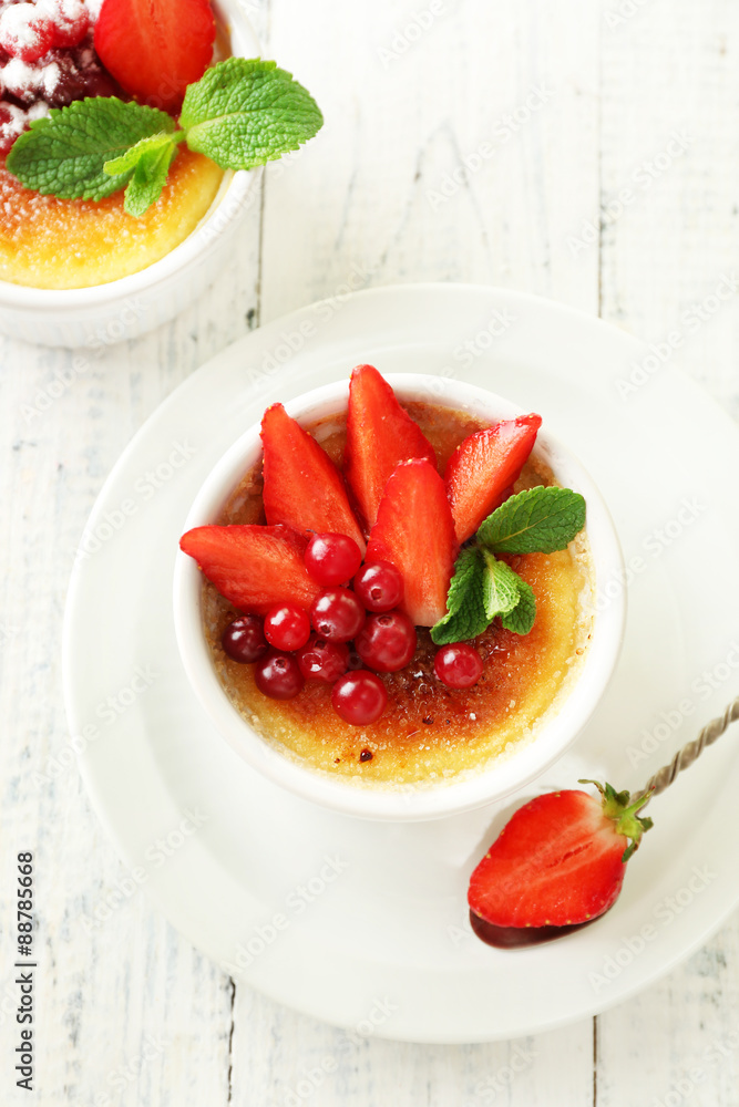 Creme brulee dessert with fresh strawberries and mint leaves, on color wooden background Creme brulee dessert with fresh strawberries and mint leaves, on color wooden background