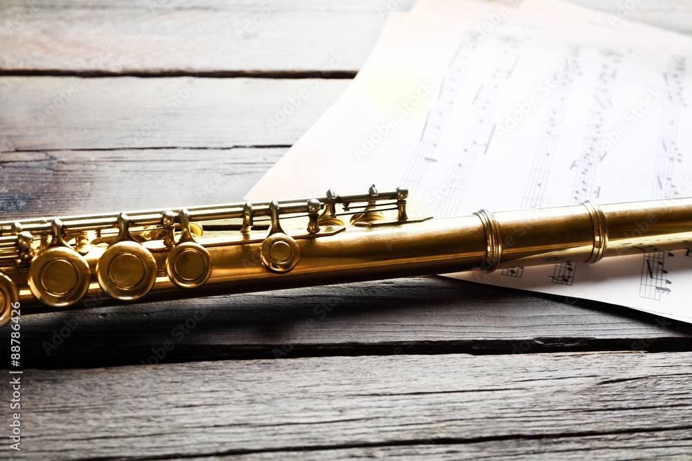 Obraz premium Silver flute with music notes on wooden table close up