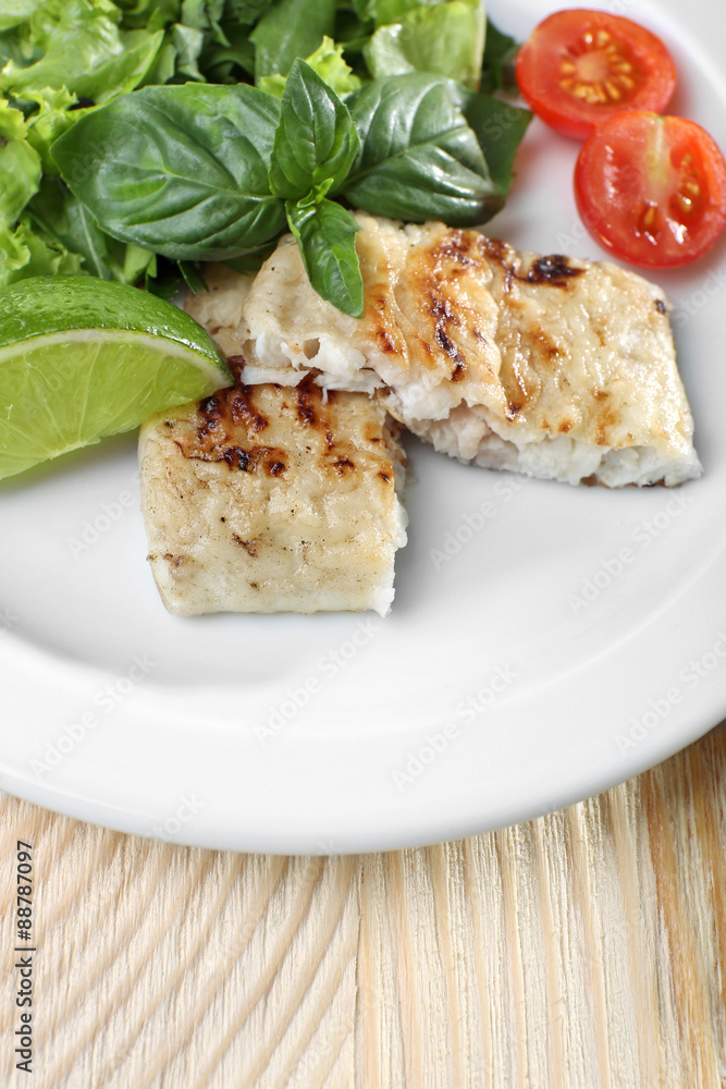 Dish of fish fillet with salad and lime on table close up Dish of fish fillet with salad and lime on table close up