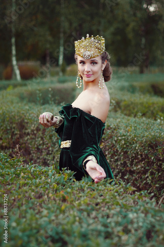 Elegant young woman dressed like queen walking in garden