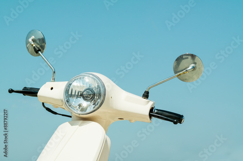 Detail of classic off-white scooter with headlight, handlebar and mirrors against blue sky