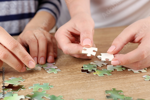 Female hands assembling puzzle on wooden table, closeup