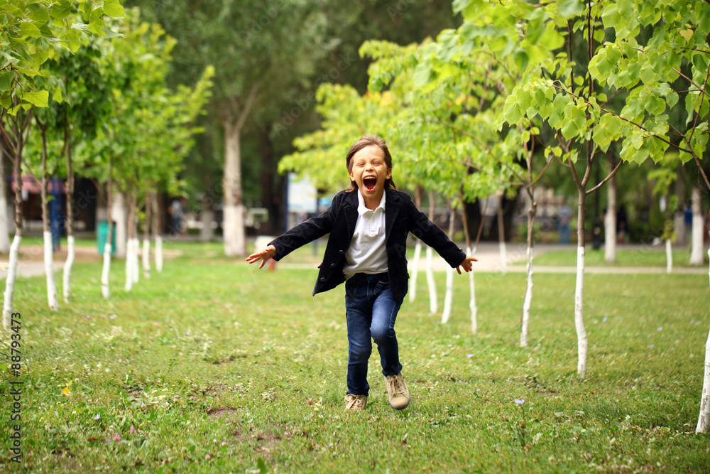 Happy little brunette boy runs in a summer park Happy little brunette boy runs in a summer park
