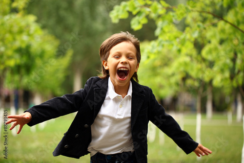 Happy little brunette boy runs in a summer park