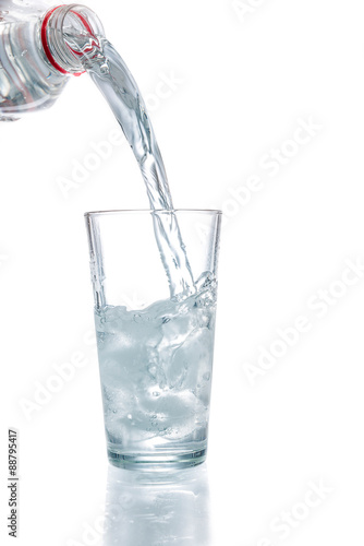 Trinkwasser aus einer Flasche in ein Glas mit Eiswürfeln gieße