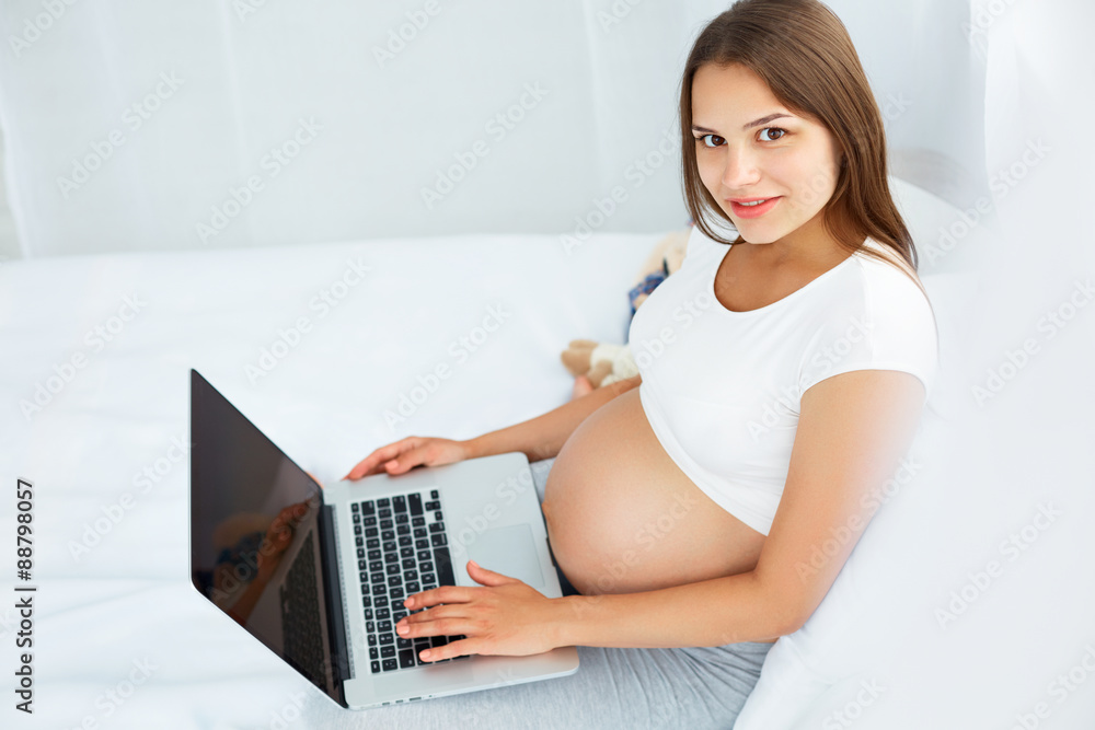 Fototapeta premium Pregnant Woman With Laptop Computer. Beautiful Pregnant Woman Working on Laptop at Home