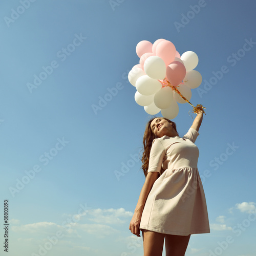 Fashion girl with  air balloons over blue sky, image toned.