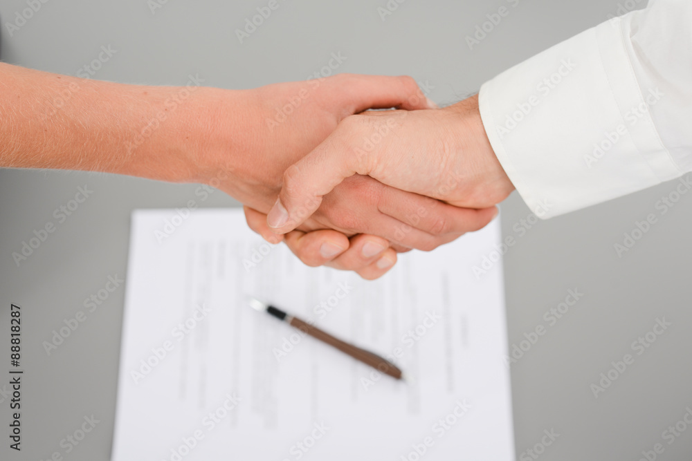 close-up shot of hands handshaking with a signed contract on the desk in background close-up shot of hands handshaking with a signed contract on the desk in background