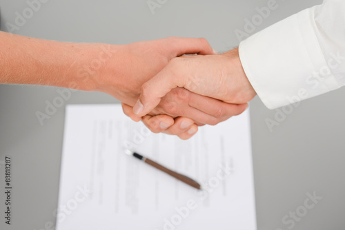 close-up shot of hands handshaking with a signed contract on the desk in background photo