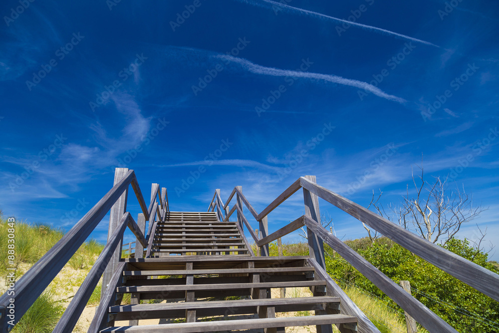 Wooden staircase and blue sky among dunes and high grass
