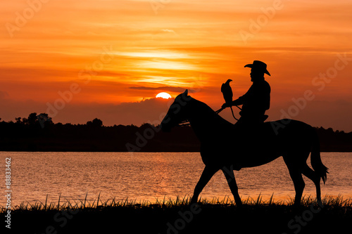 silhouette of Cowboy sitting on his horse at river sunset backgr