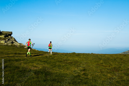 two ultra runners with backpacks and poles running on the trail in the mountains 
