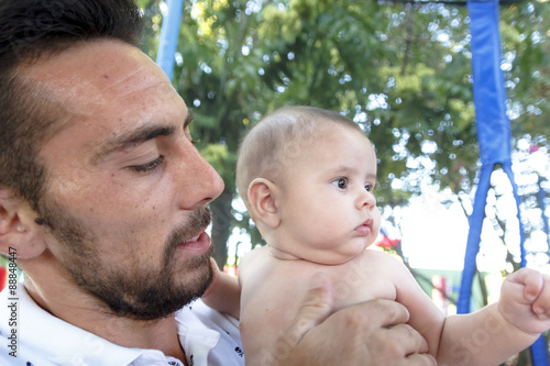 Bebe en brazos de su padre jugando en el parque. Primer plano de un padre jugando con su bebe desnudo en pañal. Bebe feliz. photo