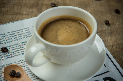 White cup of Espresso with Newspaper on the wooden table in the