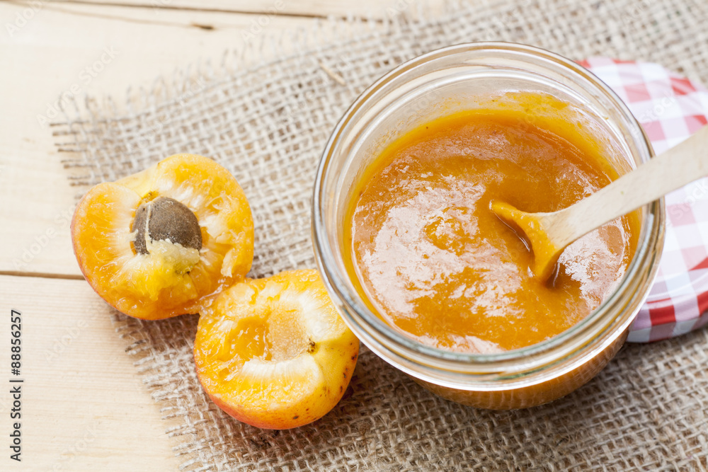 Homemade apricot jam and fresh apricots with leaves on the wooden table