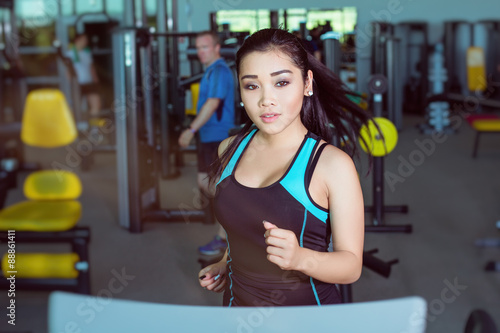 Attractive asian girl running on the treadmill in the gym. Left profile face shot
