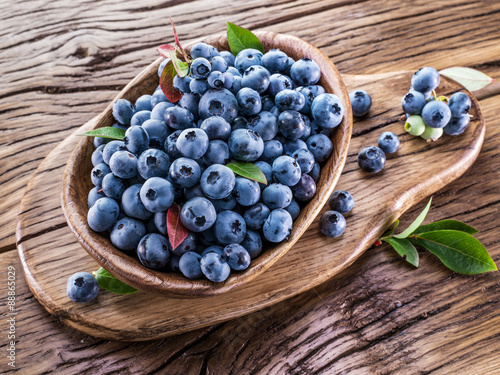 Ripe blueberries in the bowl on the wooden table.