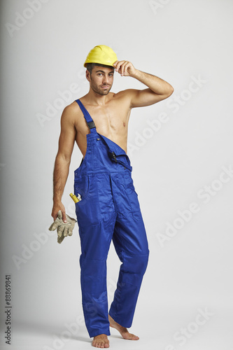 Halbnackter Handwerker mit Helm hält seine Handschue in der Hand