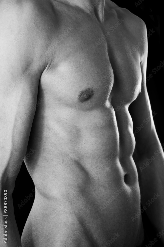 The torso of a lean but muscular young man. In black and white.  Black studio background.