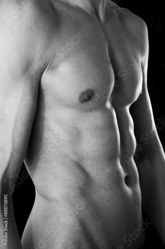 The torso of a lean but muscular young man. In black and white. Black studio background.
