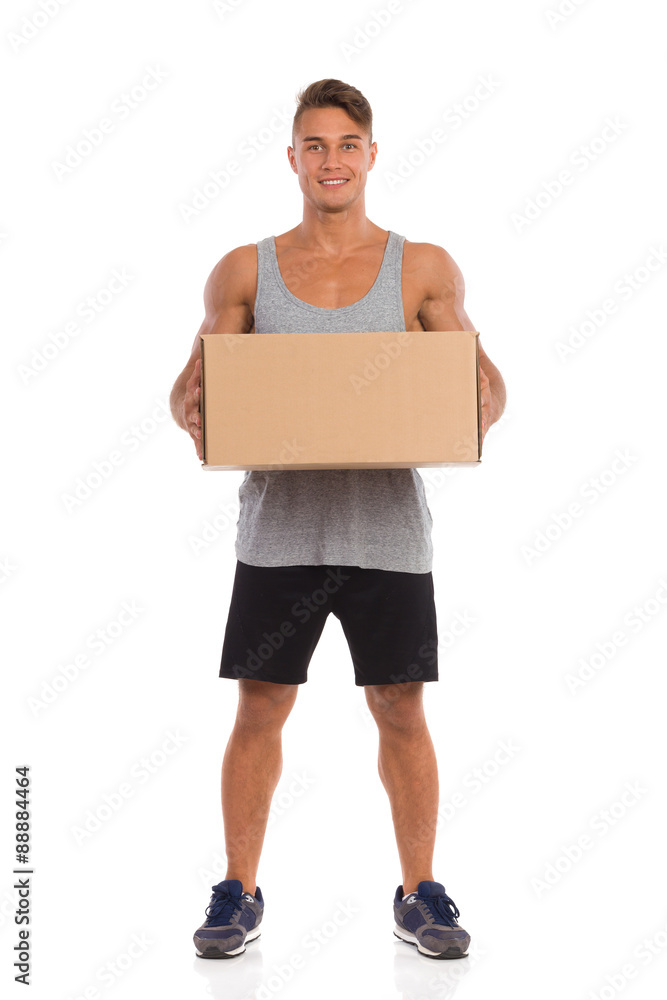 I Have Delivery For You. Smiling young man in black shorts and sneakers standing with legs apart and holding carton box. Full length studio shot isolated on white. I Have Delivery For You. Smiling young man in black shorts and sneakers standing with legs apart and holding carton box. Full length studio shot isolated on white.