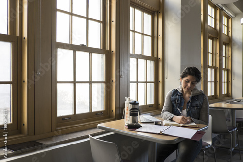Young Hispanic woman studying near windows