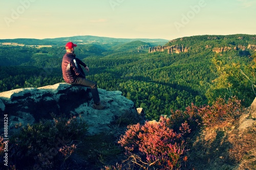 Fototapeta Naklejka Na Ścianę i Meble -  Hiker in black with red baseball cap on sharp  cliff and watch to valley. Colorful summer day.