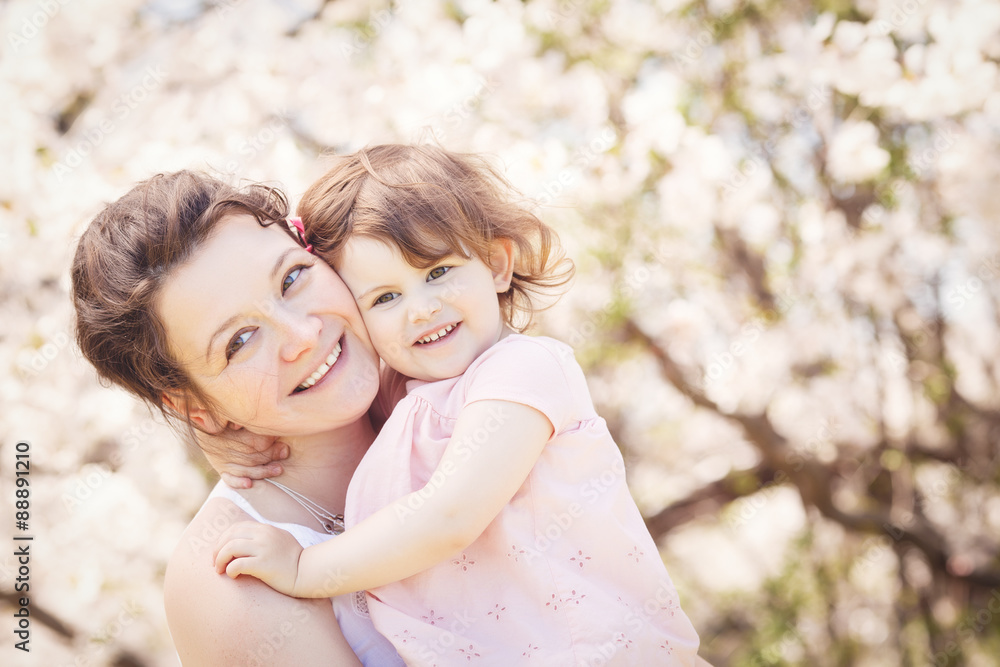 Close up portrait of caucasian mother in white dress holding hugging her daughter in pink clothes smiling on sunny spring summer day in park outside Close up portrait of caucasian mother in white dress holding hugging her daughter in pink clothes smiling on sunny spring summer day in park outside