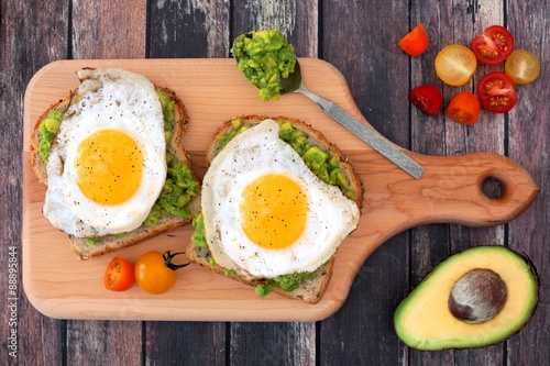 Avocado, egg open sandwiches on whole grain bread with tomatoes on paddle board on rustic wood table photo