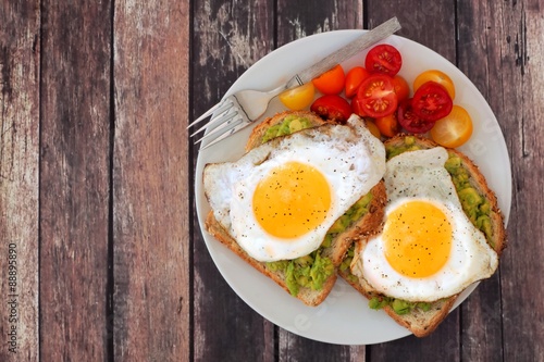 Healthy avocado, egg open sandwiches on a plate with colorful tomatoes against rustic wood
