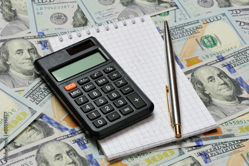 Calculator, pen and notepad on dollars