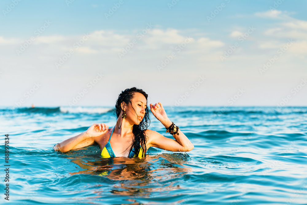 Beautiful brunette in the sea at sunset