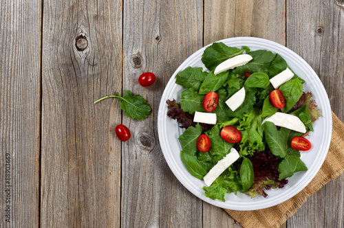 Healthy green salad on white plate with rustic wooden boards