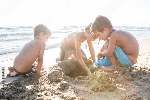Tre bambini che giocano con la sabbia in riva al mare, controluce