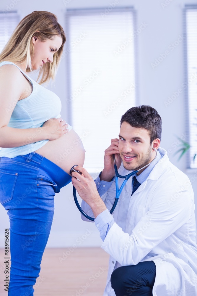 Fototapeta premium Portrait of smiling doctor examining stomach of standing pregnant woman