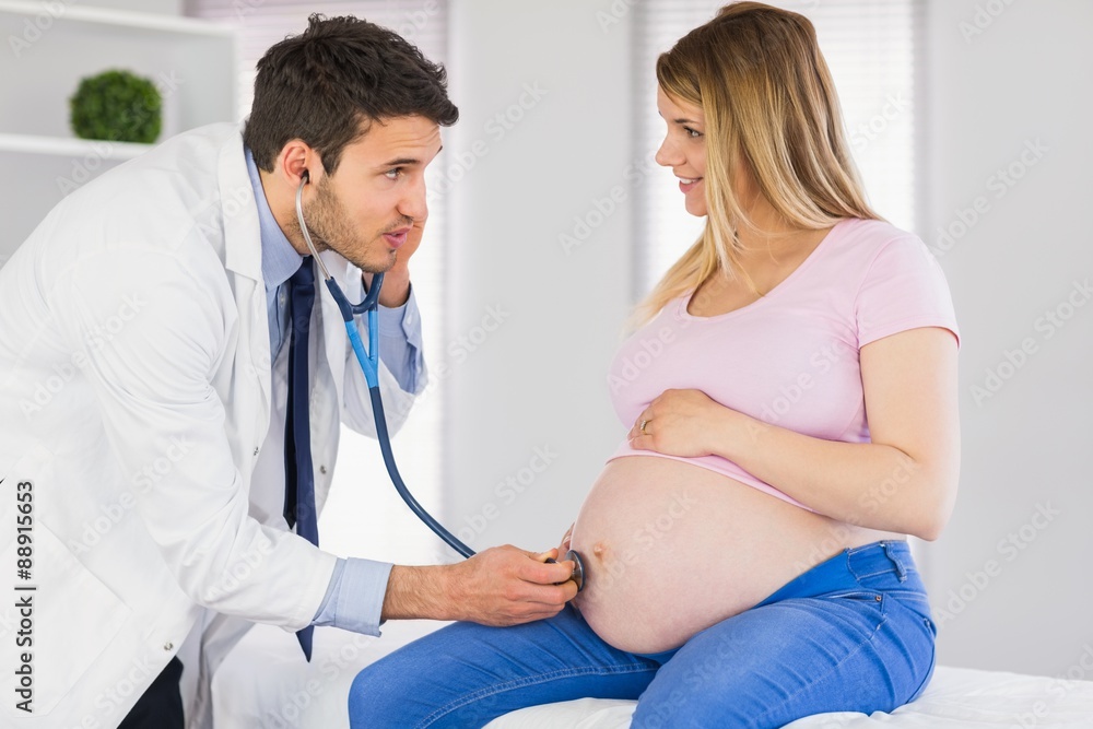 Doctor talking to pregnant patient while examining her stomach Doctor talking to pregnant patient while examining her stomach