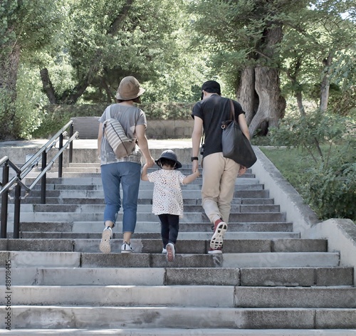 Young family - father, mother and their daughter holding hand and walking up stairs in the park, soft tone.