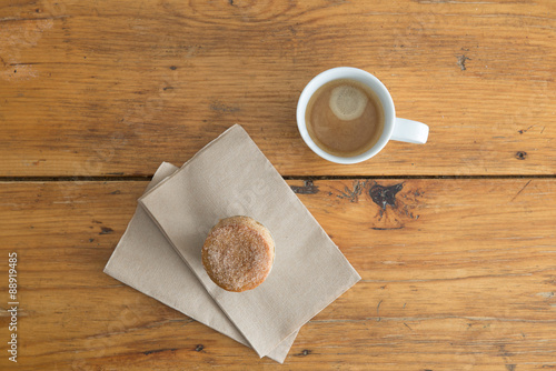 Overhead view of a fresh, sugar topped muffin and a white cup of coffee on a rustic wooden cafe table.