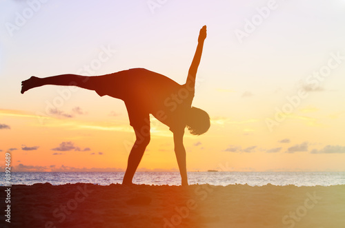 Silhouette of young man doing yoga at sunset