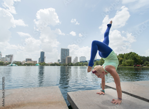 Woman doing yoga poses near a lake with city in background.