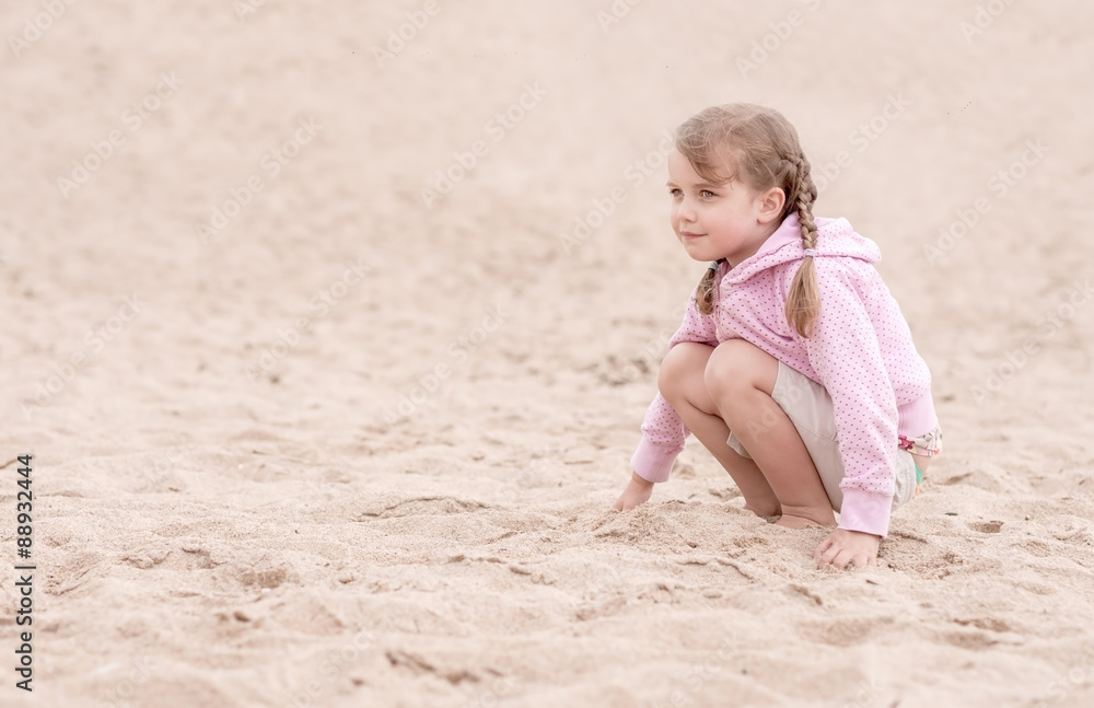 little girl kneeling on the sand and looking ahead